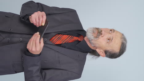 Vertical-video-of-Stressed-old-businessman,-phone-in-hand-and-indecisive-expression.
